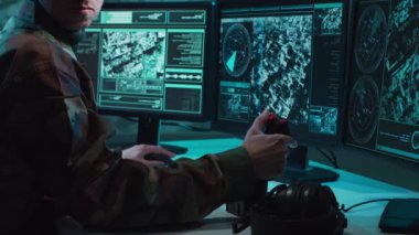 Bir askerin loş bir askeri kontrol odasındaki dramatik sahnesi, yoğun bir şekilde birden fazla bilgisayar ekranına odaklanmış, çok önemli operasyonel verileri gösteriyor..