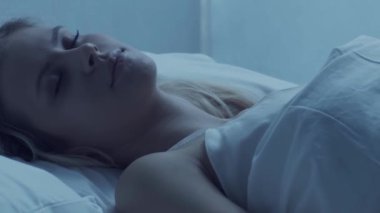 Genç bir kadın geceleri yatakta uzanıyor ve uykusuzluk hastalığına yakalanıyor. Güzel sarışın, uyuyan kız. Yatak odasında alacakaranlık, pencereden ay ışığı. Uykusuzluk, sağlık ve dinlenme konsepti. Ev