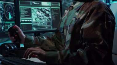 Bir askerin loş bir askeri kontrol odasındaki dramatik sahnesi, yoğun bir şekilde birden fazla bilgisayar ekranına odaklanmış, çok önemli operasyonel verileri gösteriyor..