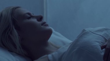 Genç bir kadın geceleri yatakta uzanıyor ve uykusuzluk hastalığına yakalanıyor. Güzel sarışın, uyuyan kız. Yatak odasında alacakaranlık, pencereden ay ışığı. Uykusuzluk, sağlık ve dinlenme konsepti. Ev