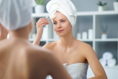 Genç Kız, Tuvalette Makyaj Aynası 'nın önünde oturuyor ve cilt kremi sürüyor. Güzel kadın kozmetik yenileme prosedürleri uyguluyor. Sağlık ve Güzellik Konsepti.