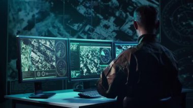 Bir askerin loş bir askeri kontrol odasındaki dramatik sahnesi, yoğun bir şekilde birden fazla bilgisayar ekranına odaklanmış, çok önemli operasyonel verileri gösteriyor..