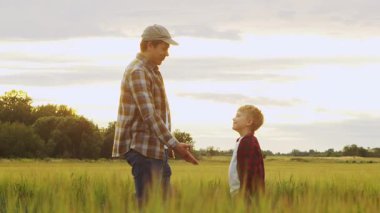 Farmer and his son in front of a sunset agricultural landscape. Man and a boy in a countryside field. The concept of fatherhood, country life, farming and country lifestyle.