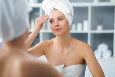 Genç Kız, Tuvalette Makyaj Aynası 'nın önünde oturuyor ve cilt kremi sürüyor. Güzel kadın kozmetik yenileme prosedürleri uyguluyor. Sağlık ve Güzellik Konsepti.