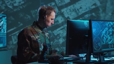 Bir askerin loş bir askeri kontrol odasındaki dramatik sahnesi, yoğun bir şekilde birden fazla bilgisayar ekranına odaklanmış, çok önemli operasyonel verileri gösteriyor..