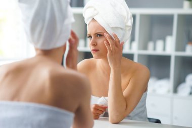 Genç Kız, Tuvalette Makyaj Aynası 'nın önünde oturuyor ve cilt kremi sürüyor. Güzel kadın kozmetik yenileme prosedürleri uyguluyor. Sağlık ve Güzellik Konsepti.