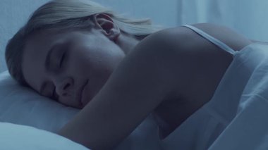 Genç bir kadın geceleri yatakta uzanıyor ve uykusuzluk hastalığına yakalanıyor. Güzel sarışın, uyuyan kız. Yatak odasında alacakaranlık, pencereden ay ışığı. Uykusuzluk, sağlık ve dinlenme konsepti. Ev