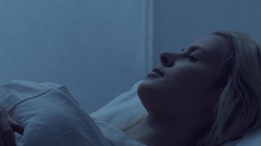 Genç bir kadın geceleri yatakta uzanıyor ve uykusuzluk hastalığına yakalanıyor. Güzel sarışın, uyuyan kız. Yatak odasında alacakaranlık, pencereden ay ışığı. Uykusuzluk, sağlık ve dinlenme konsepti. Ev