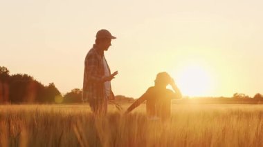 Farmer and his son in front of a sunset agricultural landscape. Man and a boy in a countryside field. The concept of fatherhood, country life, farming and country lifestyle.
