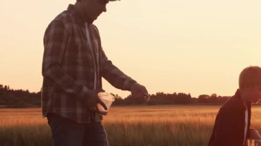 Farmer and his son in front of a sunset agricultural landscape. Man and a boy in a countryside field. The concept of fatherhood, country life, farming and country lifestyle.