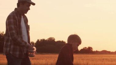 Çiftçi ve oğlu günbatımı tarımının önünde. Kırsalda bir adam ve bir çocuk. Babalık kavramı, köy hayatı, tarım ve kırsal yaşam tarzı..