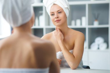 Genç Kız, Tuvalette Makyaj Aynası 'nın önünde oturuyor ve cilt kremi sürüyor. Güzel kadın kozmetik yenileme prosedürleri uyguluyor. Sağlık ve Güzellik Konsepti.