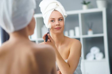 Genç Kız, Tuvalette Makyaj Aynası 'nın önünde oturuyor ve cilt kremi sürüyor. Güzel kadın kozmetik yenileme prosedürleri uyguluyor. Sağlık ve Güzellik Konsepti.