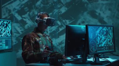 Bir askerin loş bir askeri kontrol odasındaki dramatik sahnesi, yoğun bir şekilde birden fazla bilgisayar ekranına odaklanmış, çok önemli operasyonel verileri gösteriyor..