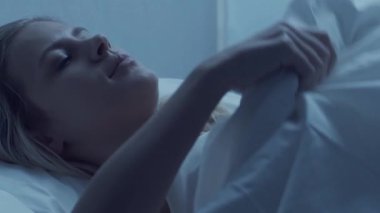 Genç bir kadın geceleri yatakta uzanıyor ve uykusuzluk hastalığına yakalanıyor. Güzel sarışın, uyuyan kız. Yatak odasında alacakaranlık, pencereden ay ışığı. Uykusuzluk, sağlık ve dinlenme konsepti. Ev