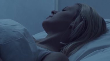 Genç bir kadın geceleri yatakta uzanıyor ve uykusuzluk hastalığına yakalanıyor. Güzel sarışın, uyuyan kız. Yatak odasında alacakaranlık, pencereden ay ışığı. Uykusuzluk, sağlık ve dinlenme konsepti. Ev