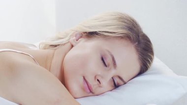 Huzurlu, huzurlu bir sahne. Genç bir kadın, rahat bir şekilde yatakta uyuyor. Yumuşak, doğal ışıklandırmayla. Rahatlama, dinlenme ve sükunet temaları için mükemmel. Ev kavramı.