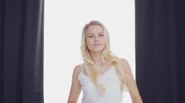 Yatakta uzanan genç kadın, büyük perdelerin arasından süzülen güneş ışığıyla çerçevelenmiş, sabah dinginliği ve gençleşme hissi uyandırıyor. Ev kavramı.