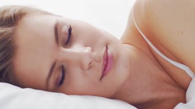 Huzurlu, huzurlu bir sahne. Genç bir kadın, rahat bir şekilde yatakta uyuyor. Yumuşak, doğal ışıklandırmayla. Rahatlama, dinlenme ve sükunet temaları için mükemmel. Ev kavramı.