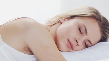 Huzurlu, huzurlu bir sahne. Genç bir kadın, rahat bir şekilde yatakta uyuyor. Yumuşak, doğal ışıklandırmayla. Rahatlama, dinlenme ve sükunet temaları için mükemmel. Ev kavramı.