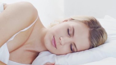 Huzurlu, huzurlu bir sahne. Genç bir kadın, rahat bir şekilde yatakta uyuyor. Yumuşak, doğal ışıklandırmayla. Rahatlama, dinlenme ve sükunet temaları için mükemmel. Ev kavramı.