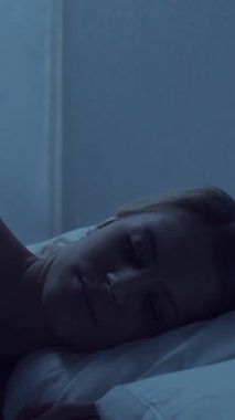 Genç bir kadın geceleri yatakta uzanıyor ve uykusuzluk hastalığına yakalanıyor. Güzel sarışın, uyuyan kız. Yatak odasında alacakaranlık, pencereden ay ışığı. Uykusuzluk, sağlık ve dinlenme konsepti. Dikey