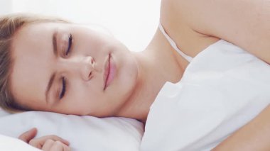 Huzurlu, huzurlu bir sahne. Genç bir kadın, rahat bir şekilde yatakta uyuyor. Yumuşak, doğal ışıklandırmayla. Rahatlama, dinlenme ve sükunet temaları için mükemmel. Ev kavramı.