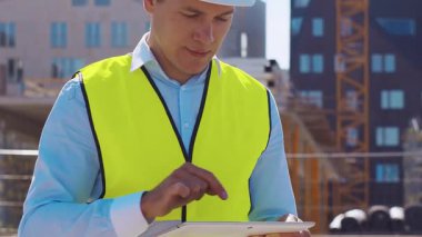 İnşaat alanının önünde duran profesyonel müteahhit. Kasklı ve yelekli ustabaşı. Ofis binası ve vinç arka planı. İş, gayrimenkul ve yatırım kavramları.