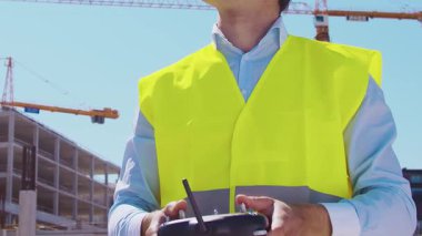 İnşaat alanının önünde duran profesyonel müteahhit. Kasklı ve yelekli ustabaşı. Ofis binası ve vinç arka planı. İş, gayrimenkul ve yatırım kavramları.