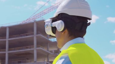 İnşaat alanının önünde duran profesyonel müteahhit. Kasklı ve yelekli ustabaşı. Ofis binası ve vinç arka planı. İş, gayrimenkul ve yatırım kavramları.