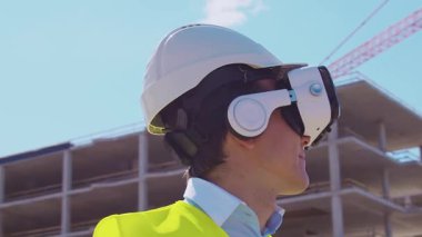 İnşaat alanının önünde duran profesyonel müteahhit. Kasklı ve yelekli ustabaşı. Ofis binası ve vinç arka planı. İş, gayrimenkul ve yatırım kavramları.