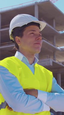 İnşaat alanının önünde duran profesyonel müteahhit. Kasklı ve yelekli ustabaşı. Ofis binası ve vinç arka planı. İş, gayrimenkul ve yatırım kavramları.