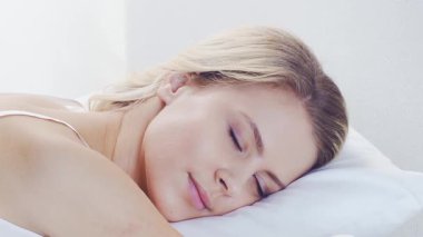 Huzurlu, huzurlu bir sahne. Genç bir kadın, rahat bir şekilde yatakta uyuyor. Yumuşak, doğal ışıklandırmayla. Rahatlama, dinlenme ve sükunet temaları için mükemmel. Ev kavramı.