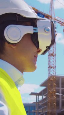 İnşaat alanının önünde duran profesyonel müteahhit. Kasklı ve yelekli ustabaşı. Ofis binası ve vinç arka planı. İş, gayrimenkul ve yatırım kavramları.