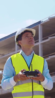 İnşaat alanının önünde duran profesyonel müteahhit. Kasklı ve yelekli ustabaşı. Ofis binası ve vinç arka planı. İş, gayrimenkul ve yatırım kavramları.