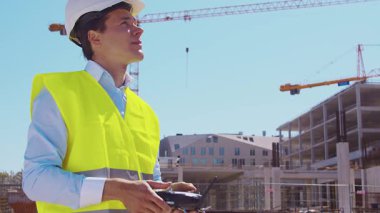 İnşaat alanının önünde duran profesyonel müteahhit. Kasklı ve yelekli ustabaşı. Ofis binası ve vinç arka planı. İş, gayrimenkul ve yatırım kavramları.