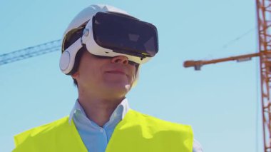 İnşaat alanının önünde duran profesyonel müteahhit. Kasklı ve yelekli ustabaşı. Ofis binası ve vinç arka planı. İş, gayrimenkul ve yatırım kavramları.