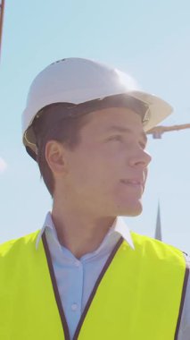 İnşaat alanının önünde duran profesyonel müteahhit. Kasklı ve yelekli ustabaşı. Ofis binası ve vinç arka planı. İş, gayrimenkul ve yatırım kavramları.