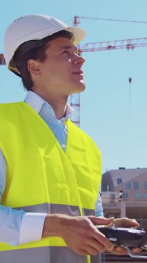 İnşaat alanının önünde duran profesyonel müteahhit. Kasklı ve yelekli ustabaşı. Ofis binası ve vinç arka planı. İş, gayrimenkul ve yatırım kavramları.