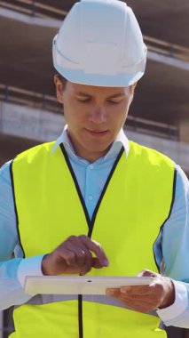 İnşaat alanının önünde duran profesyonel müteahhit. Kasklı ve yelekli ustabaşı. Ofis binası ve vinç arka planı. İş, gayrimenkul ve yatırım kavramları.