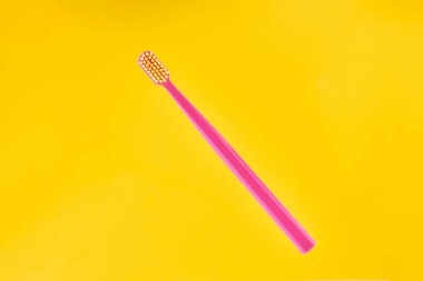 Pink toothbrush on yellow background for oral hygiene to clean teeth, gums and tongue. Manual plastic toothbrush for effective toothbrushing and healthy smile, isolated on yellow background