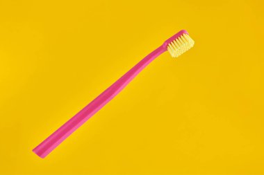 Pink toothbrush on yellow background for oral hygiene to clean teeth, gums and tongue. Manual plastic toothbrush for effective toothbrushing and healthy smile, isolated on yellow background