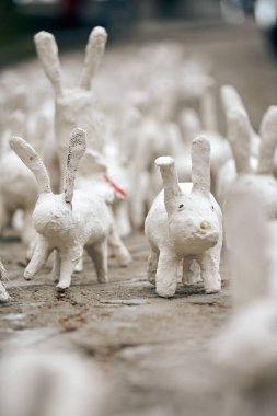 White rabbit statues made of plaster at outdoor art exhibition, artificial white hares on city street. A lot of white handmade rabbits, many decorative bunnies, Easter urban decor concept