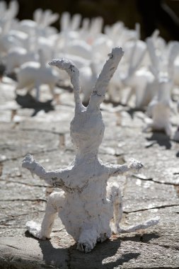 Big white rabbit statue made of plaster back view, outdoor art exhibition, artificial strange hare on city street. Handmade decorative bunny in front of flock of small rabbits, Easter urban decor