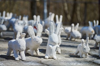 White rabbit statues made of plaster at outdoor art exhibition, artificial white hares on city street. A lot of white handmade rabbits, many decorative bunnies, Easter urban decor concept