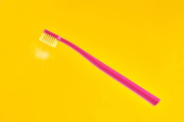 Pink toothbrush on yellow background for oral hygiene to clean teeth, gums and tongue. Manual plastic toothbrush with fresh shine near bristle isolated on yellow background