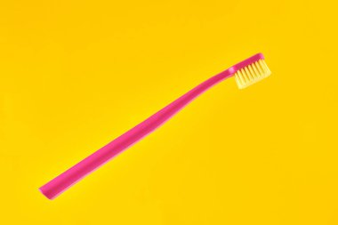 Pink toothbrush on yellow background for oral hygiene to clean teeth, gums and tongue. Manual plastic toothbrush for effective toothbrushing and healthy smile, isolated on yellow background