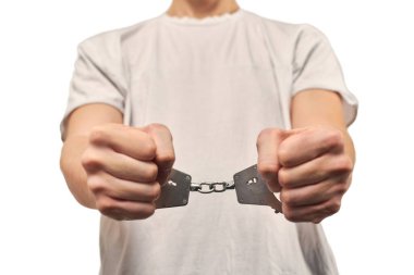 Hands of criminal in handcuffs, arrest of dangerous criminal isolated on white background, close up. Male fists locked in handcuffs, apprehension of offender in off-white T-shirt, violation of law