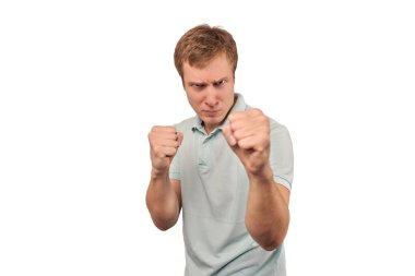 Angry young man in light grey T-shirt ready to fight with fists isolated on white background. Aggressive handsome man going to fistfight, defense gesture, bad guy with clenched fists