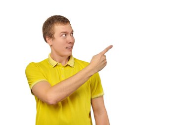 Surprised young guy with funny face in bright yellow T-shirt pointing finger to right, white isolated background. Shocked amazed face of young man in T-shirt. Portrait of excited man